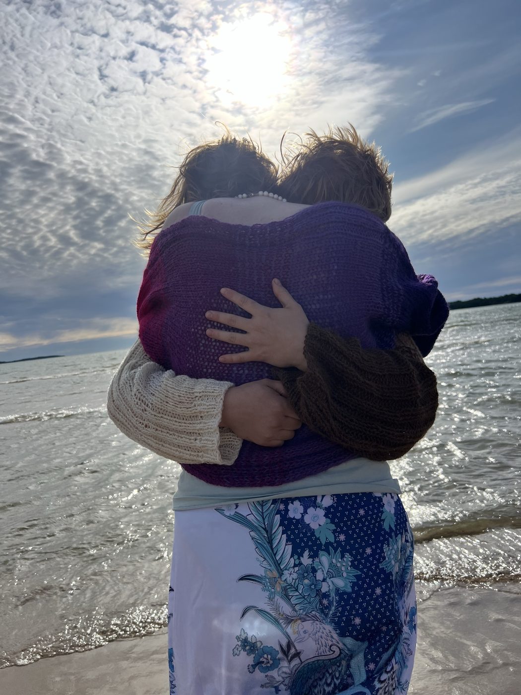 Second angle of two people hugging in Hali pullovers by the sea, sunset light