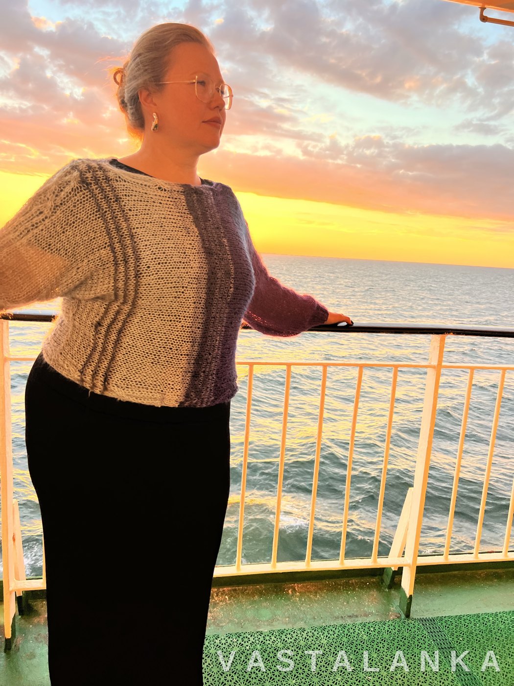 Model wearing the Hali ombre pullover in purple and pale blue, by the sea at sunset