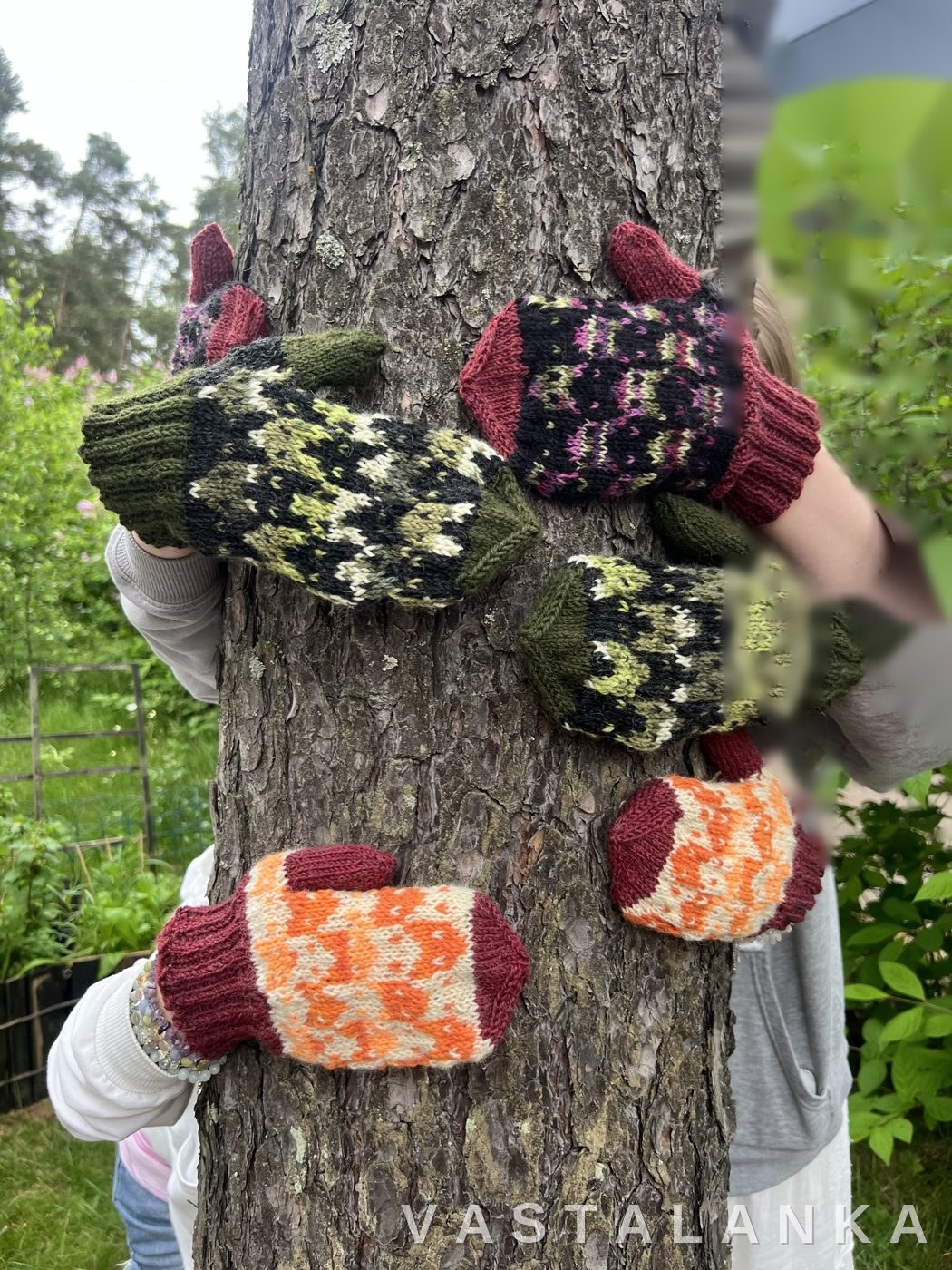 All three Kettu mitten pairs hugging a tree trunk, wide view