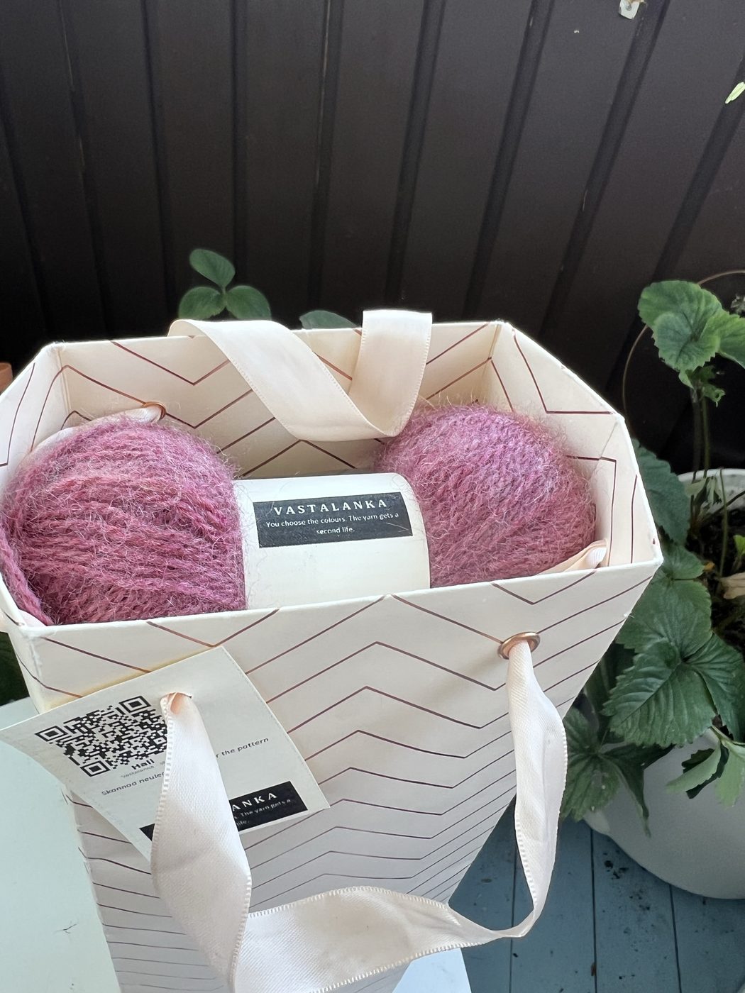 A finished Hali kit ready to ship, all balls tucked into a repurposed patterned paper bag with a printed QR hangtag