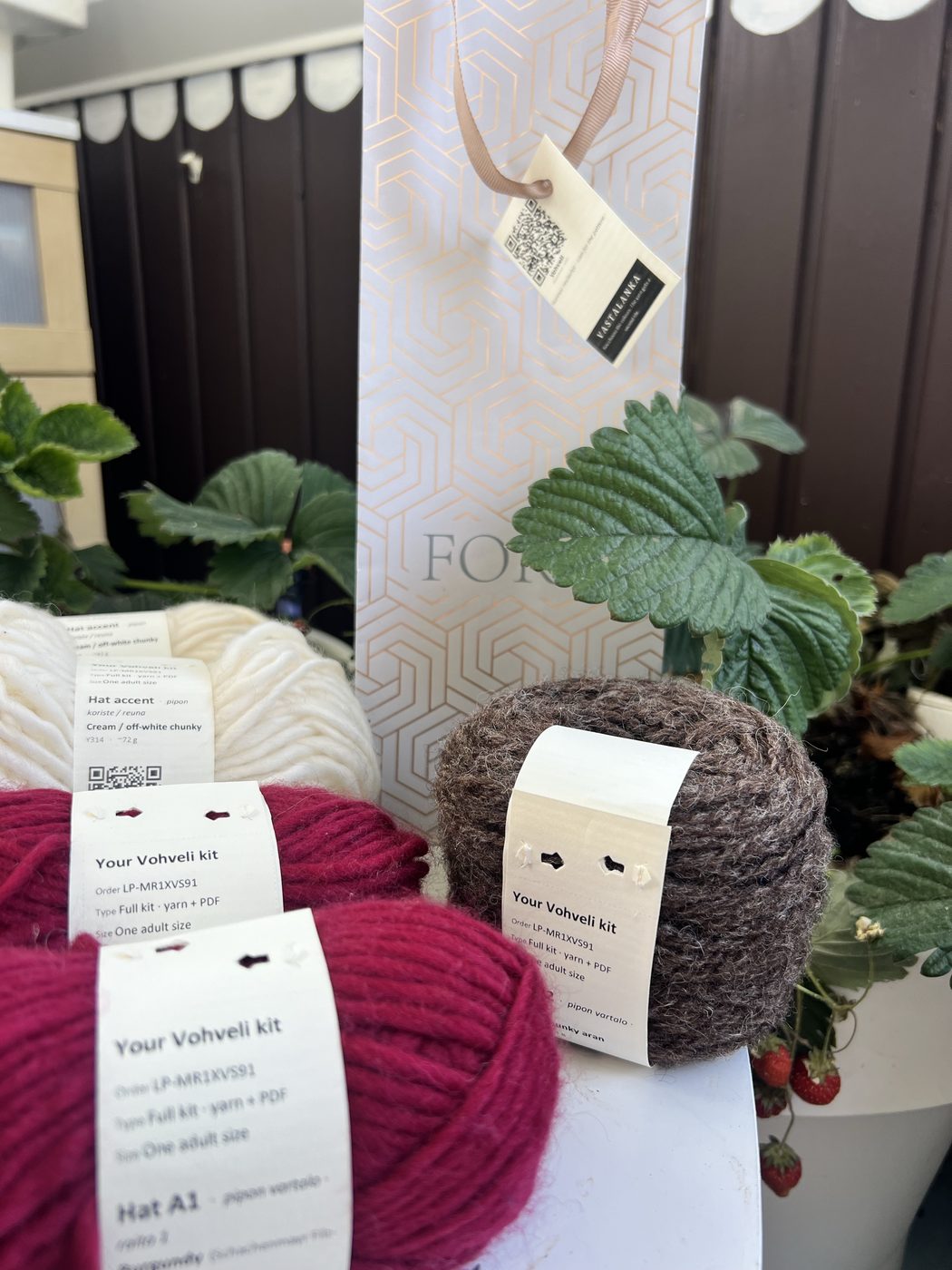A Vohveli hat kit: three wound yarn balls with printed bands for the ribbing, dome stripe and waffle accent slots, alongside a repurposed gift bag with a Vastalanka hangtag