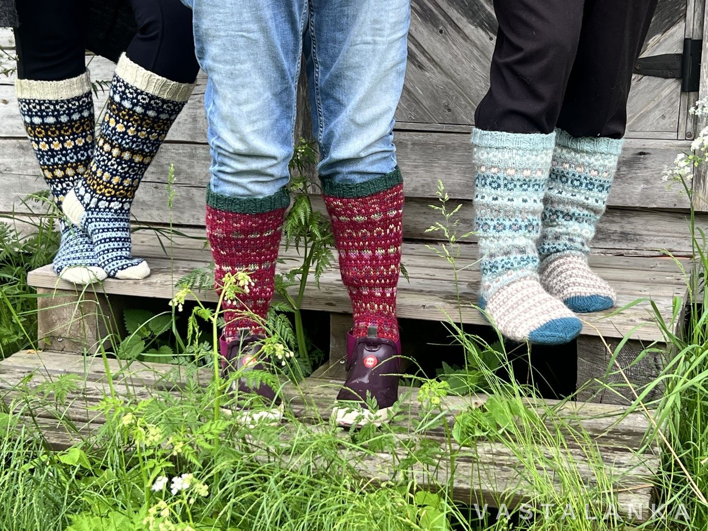 Three pairs of hand-knitted Pallukka colourwork socks worn on a wooden porch step