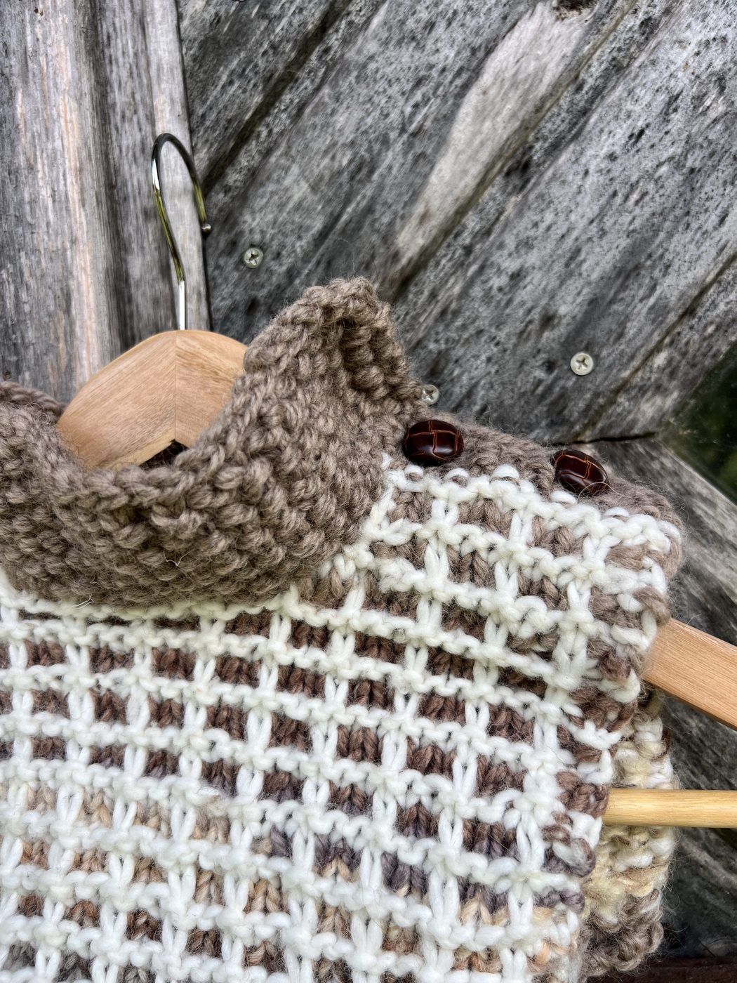 Vohveli waffle-stitch cowl in beige and cream, hanging on wooden hanger with dark buttons