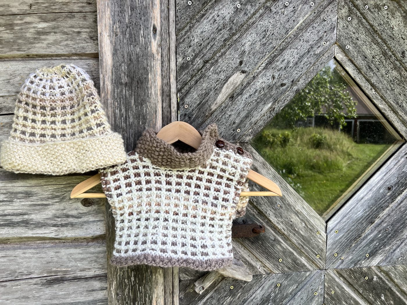 Vohveli waffle-stitch hat and cowl in beige and cream, hung together on a weathered wooden wall