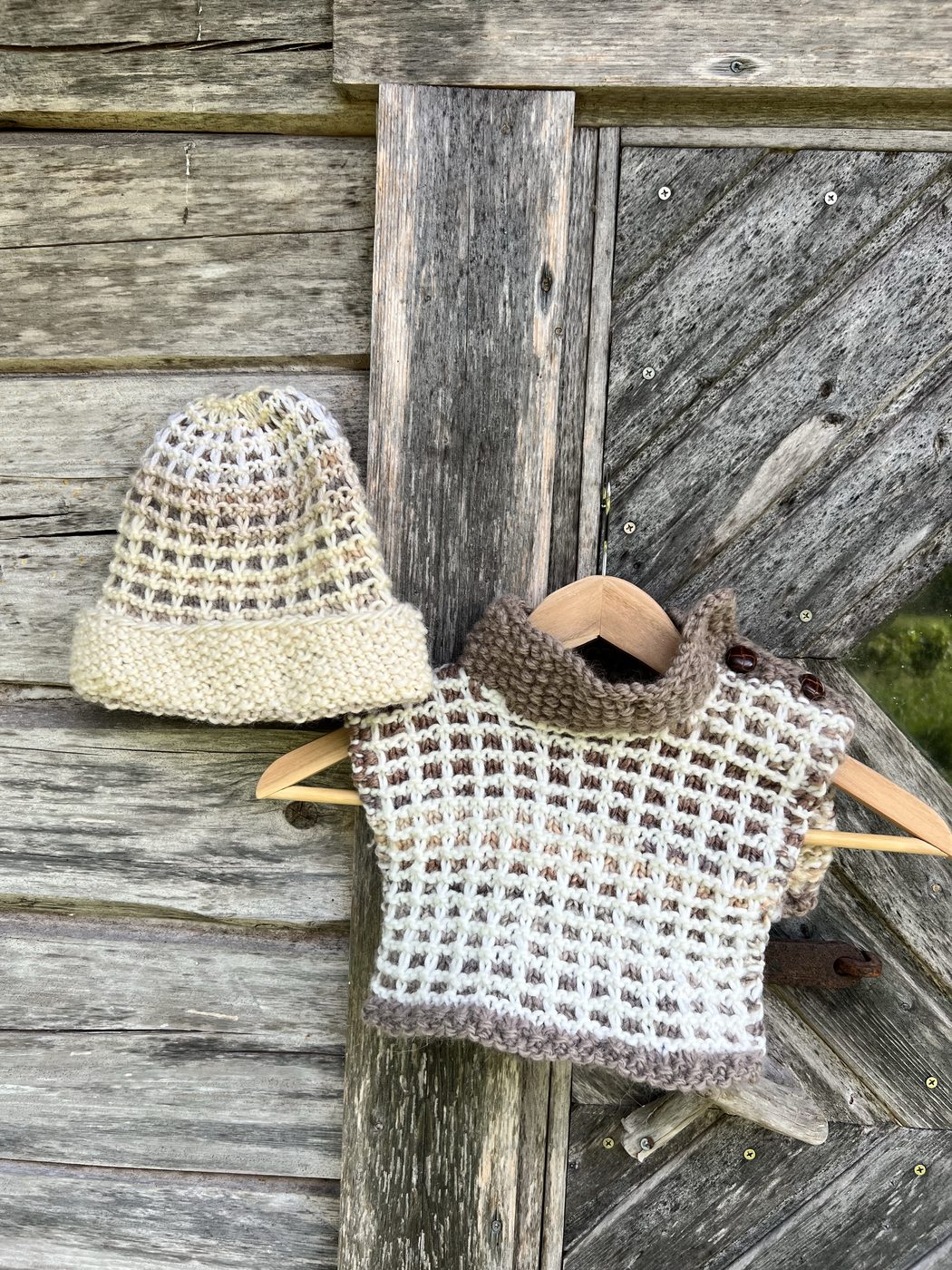 Vohveli hat and cowl in beige and cream, portrait view, hanging on weathered wooden wall