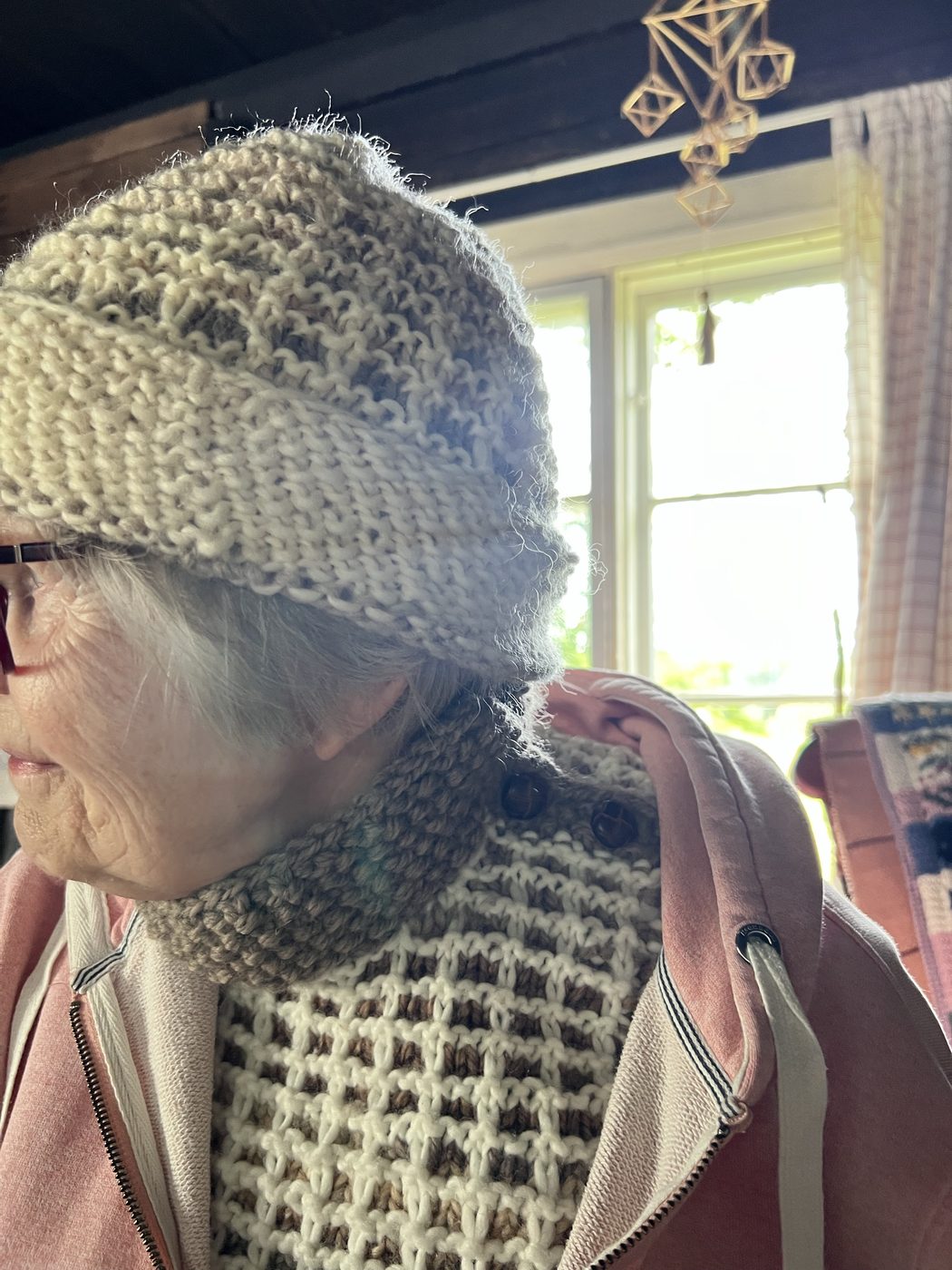 Model wearing the Vohveli hat and cowl indoors, side profile with warm daylight